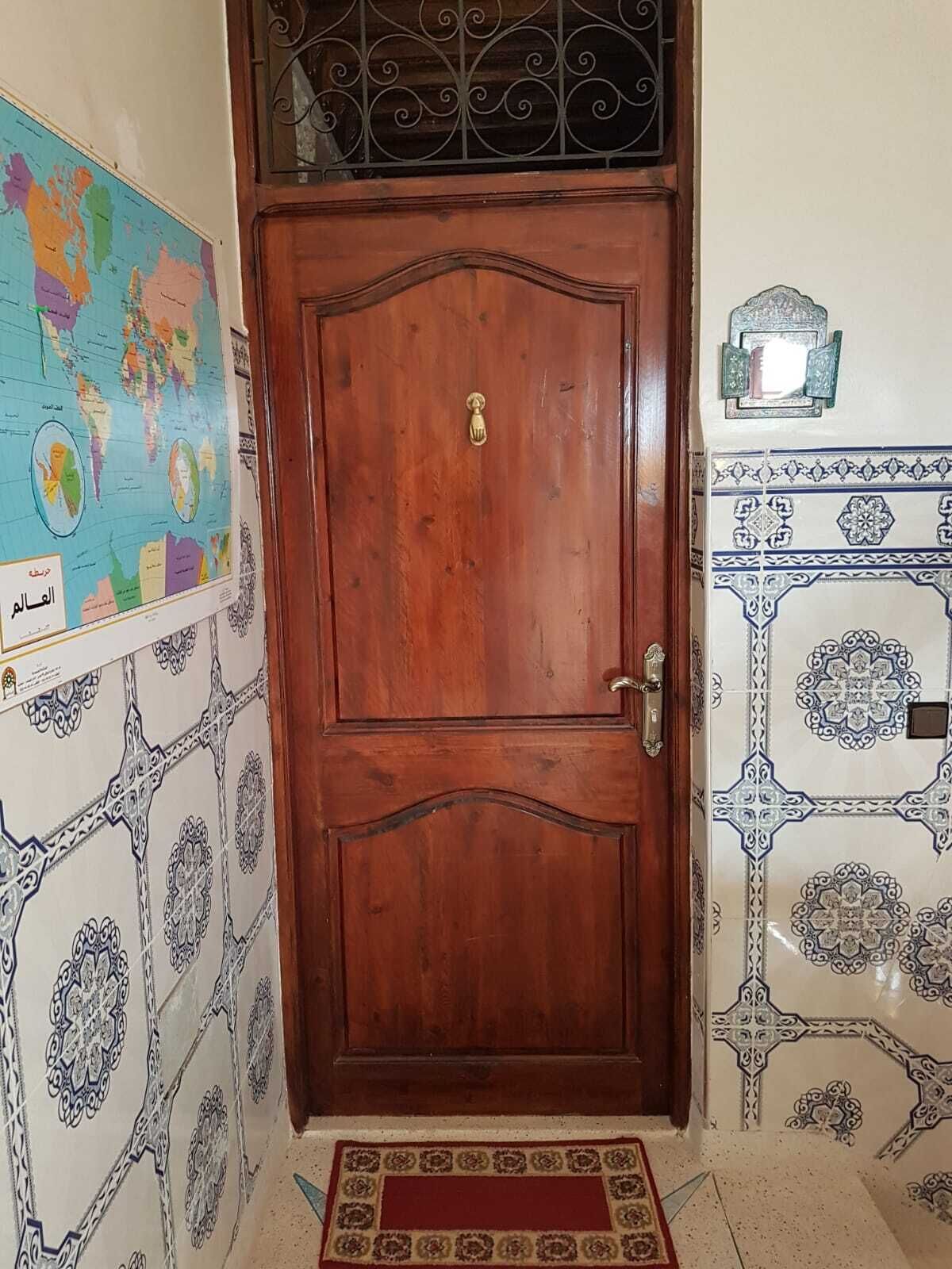 Una puerta de madera con un tirador y un picaporte de latón, flanqueada por baldosas con diseños y un mapa mundial en la pared.