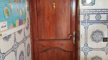 Una puerta de madera con un tirador y un picaporte de latón, flanqueada por baldosas con diseños y un mapa mundial en la pared.