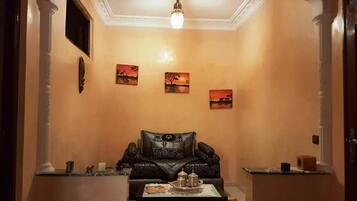 Una sala de estar con un sofá de cuero negro, una mesa de centro con objetos decorativos y tres cuadros de atardecer en la pared.