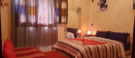 A bedroom with two beds, a window with curtains, a lamp, and a wall-mounted picture.