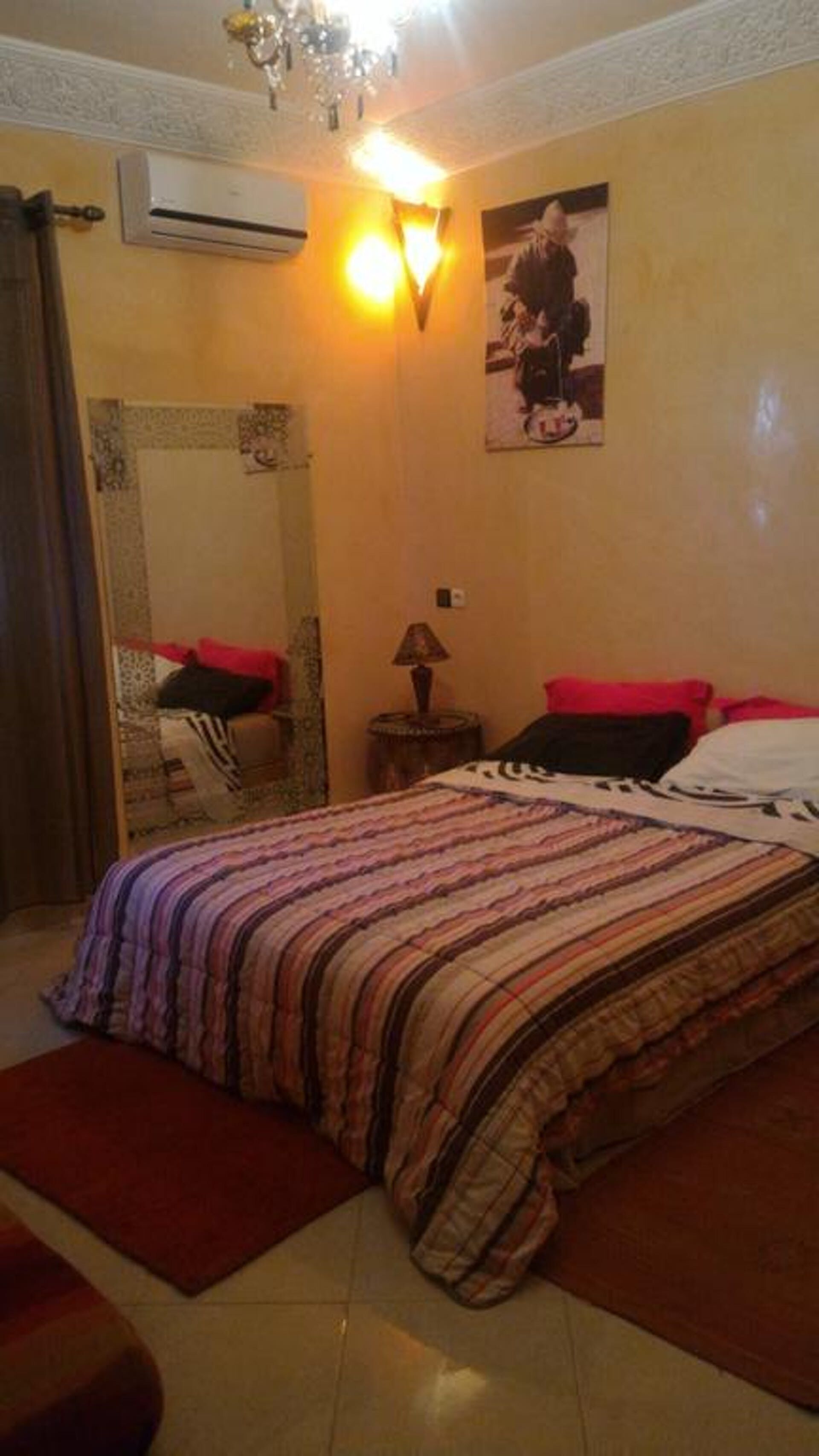 Un dormitorio con cama, mesita de noche, lámpara, espejo y aire acondicionado de pared.