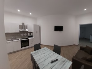A modern kitchen with white cabinets, a microwave, and a stove. There is a dining table with chairs and a remote control on it.