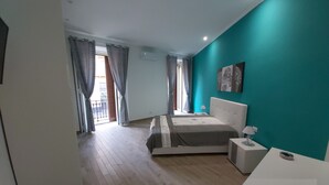 A bedroom with a bed, a nightstand, a lamp, a window with curtains, and a teal accent wall. - Dormire a Napoli Centro Holiday House (Naples)