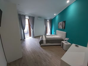 Ett sovrum med en säng, ett sängbord, en lampa, ett fönster med gardiner och en vägg som är accentfärgad i turkos.