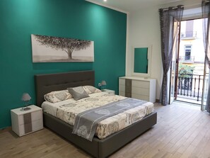 A bedroom with a bed, bedside tables, a dresser, a mirror, and a balcony with a view.