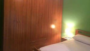 A bedroom with a large wooden wardrobe, a bed with white bedding, and a nightstand with a lamp.
