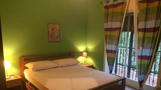 A single bed with a wooden frame, two bedside lamps, a small bedside table, and a window with striped curtains.