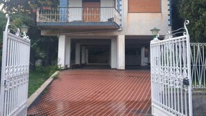 A two-story house with a balcony, a gated entrance, and a paved driveway.