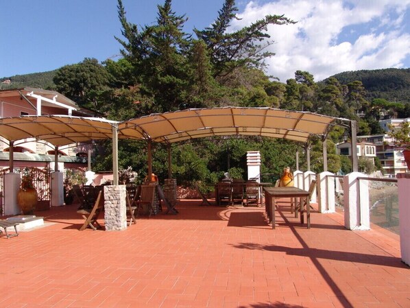 An outdoor patio area with a covered seating area, stone pillars, and a view of the surrounding landscape. - Locanda Il Senatore (Lerici)