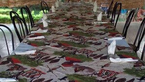 Uma longa mesa de jantar com toalha de mesa estampada, rodeada por cadeiras de metal.