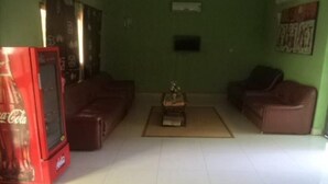 Uma sala de estar com um refrigerador vermelho Coca-Cola, dois sofás marrons, uma mesa de centro e uma TV de tela plana na parede.