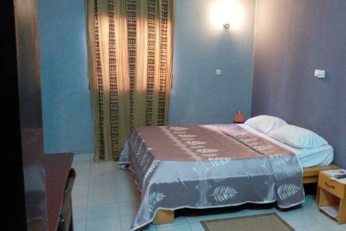 A small, well-lit bedroom with a single bed, a nightstand, and a curtain.