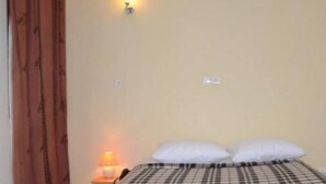 Quarto com cama, ar-condicionado na parede, mesa de cabeceira com abajur e cortina.