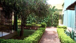 Um caminho no jardim com piso de azulejos, cercado por vegetação exuberante e um pequeno lago.