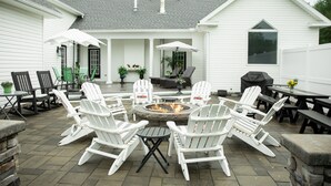 Uma área de pátio com cadeiras Adirondack brancas, um braseiro e uma mesa coberta.