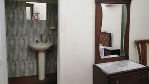 A bathroom with a marble-patterned wall, a pedestal sink, a mirror with a wooden frame, and a wooden nightstand. - New Hotel (Cairo)