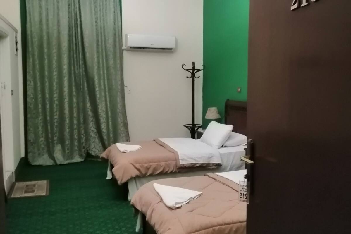 Ein Hotelzimmer mit zwei Betten, einer grünen Wand, einer Chandelüster, einer Klimaanlage und einer Tür mit der Aufschrift 215.