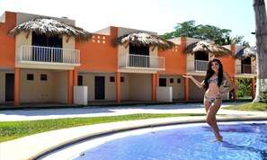 Ein Hotel mit reetgedeckten Balkonen, einem Pool und einer tropischen Umgebung.
