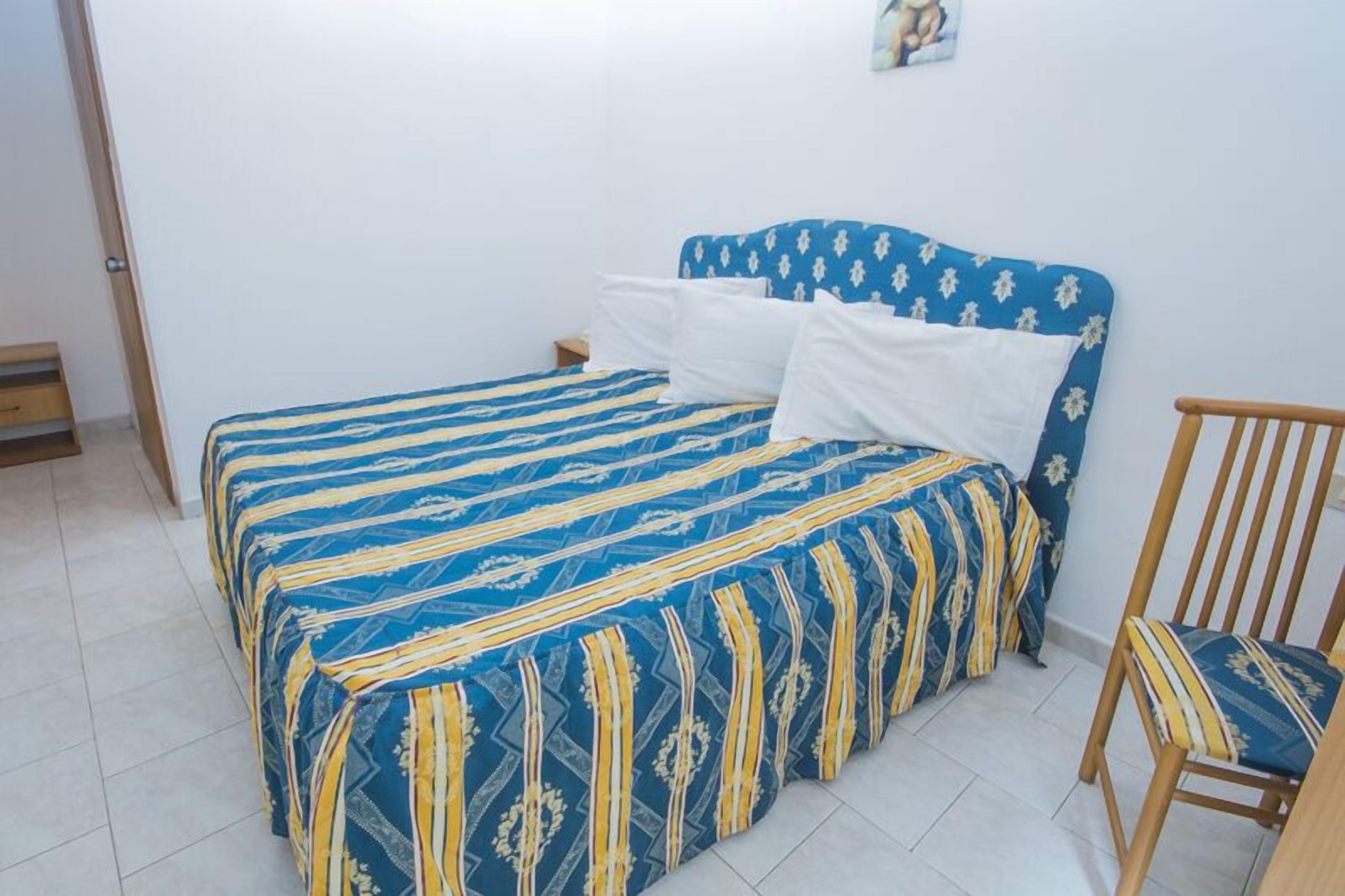 Una camera da letto con un letto coperto da una coperta a righe blu e gialle, una sedia di legno e un comodino.
