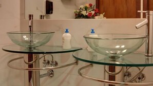 A bathroom with two glass sinks, a mirror, a wooden door, and a marble wall. - Hotel Ambrogini (Montecatini Terme)