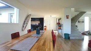 A spacious dining area with a long wooden table and red chairs, a kitchen in the background, and a staircase leading to another level. - Top villa for families: pool, games, aperitifs, beaches and mountains nearby! (Villefranque)