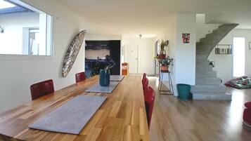 Ruime eethoek met een lange houten tafel en rode stoelen, een keuken achtergrond en een trap naar een ander niveau.