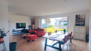 A modern living room with a large TV, red sofa, dining table, and potted plants. - Top villa for families: pool, games, aperitifs, beaches and mountains nearby! (Villefranque)