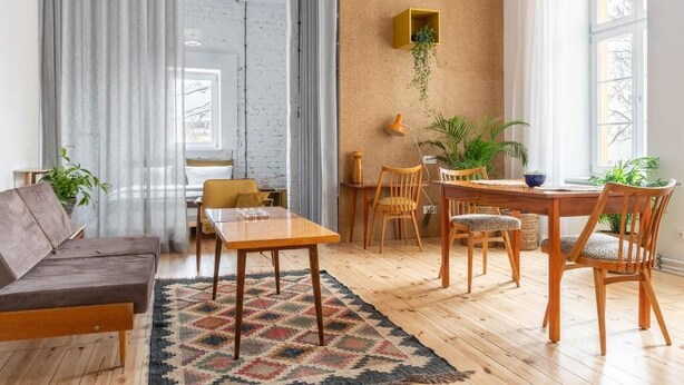 A modern living room with a sofa, dining table, chairs, and a coffee table. There is a window with curtains, a brick wall, and a corkboard with a plant. - Visitting Apartments - Podwale (Wroclaw)