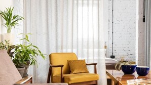 A modern living room with a mustard-colored armchair, a wooden coffee table, and a white brick wall. - Visitting Apartments - Podwale (Wroclaw)