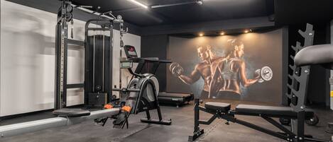 A gym with exercise equipment, a treadmill, and a wall with a muscular figure.