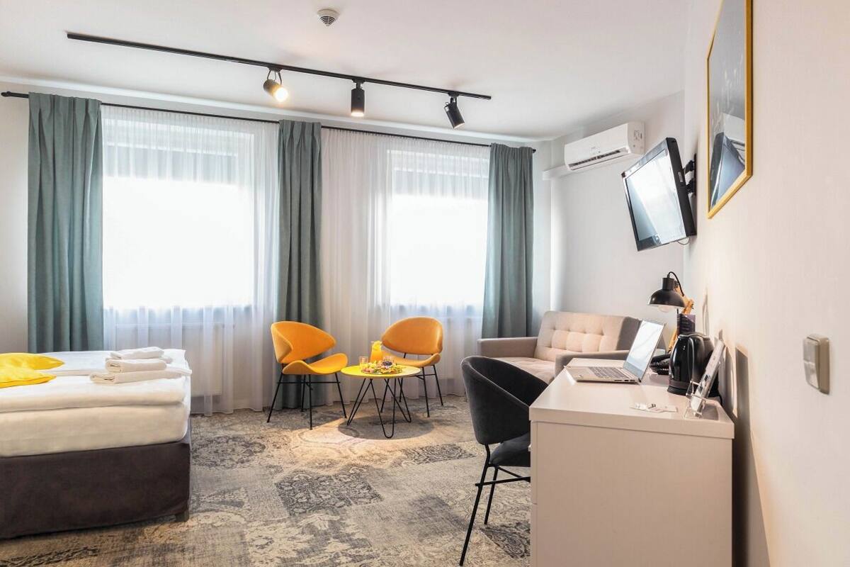 A hotel room with a bed, desk, two chairs, a sofa, and a TV.