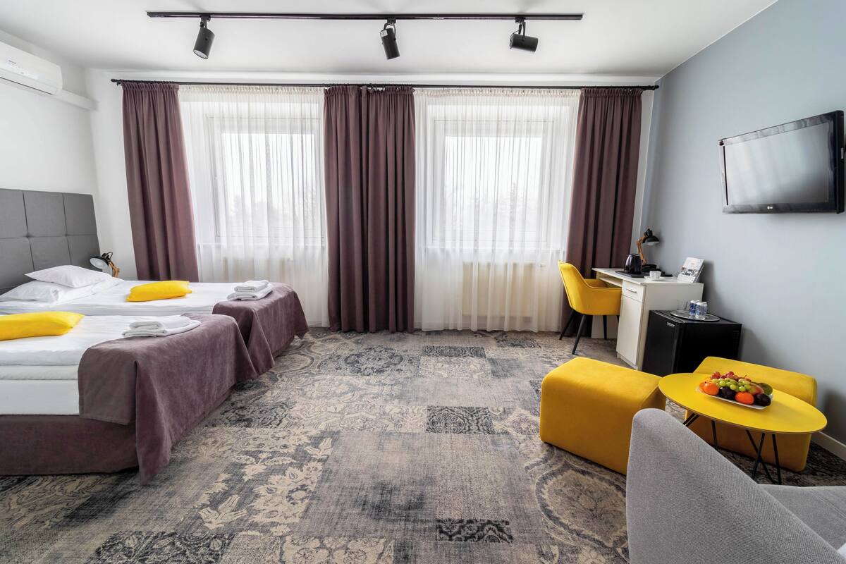A hotel room with two beds, a desk, a chair, a TV, and a small table with fruit.
