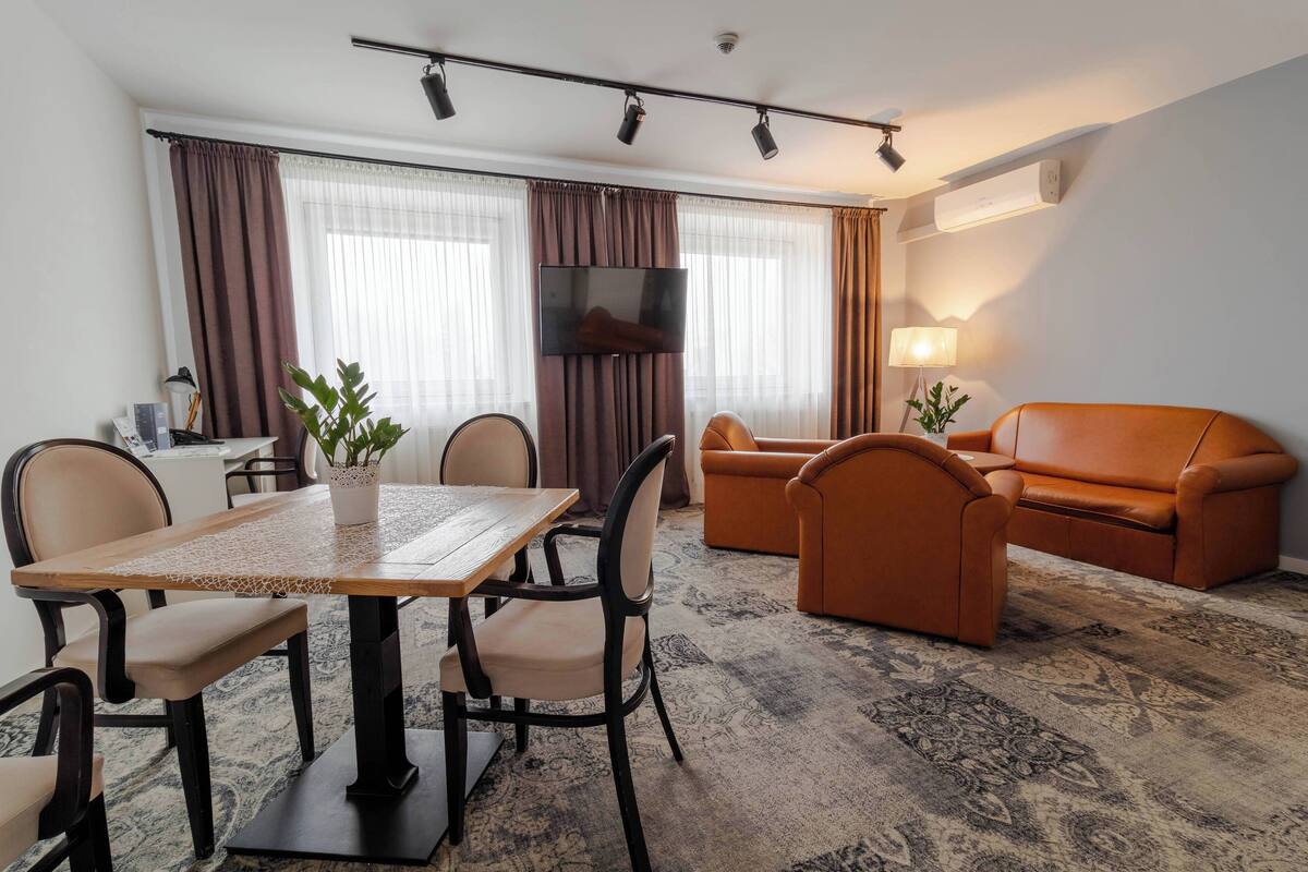 A hotel room with a dining table, chairs, a sofa, and a TV.