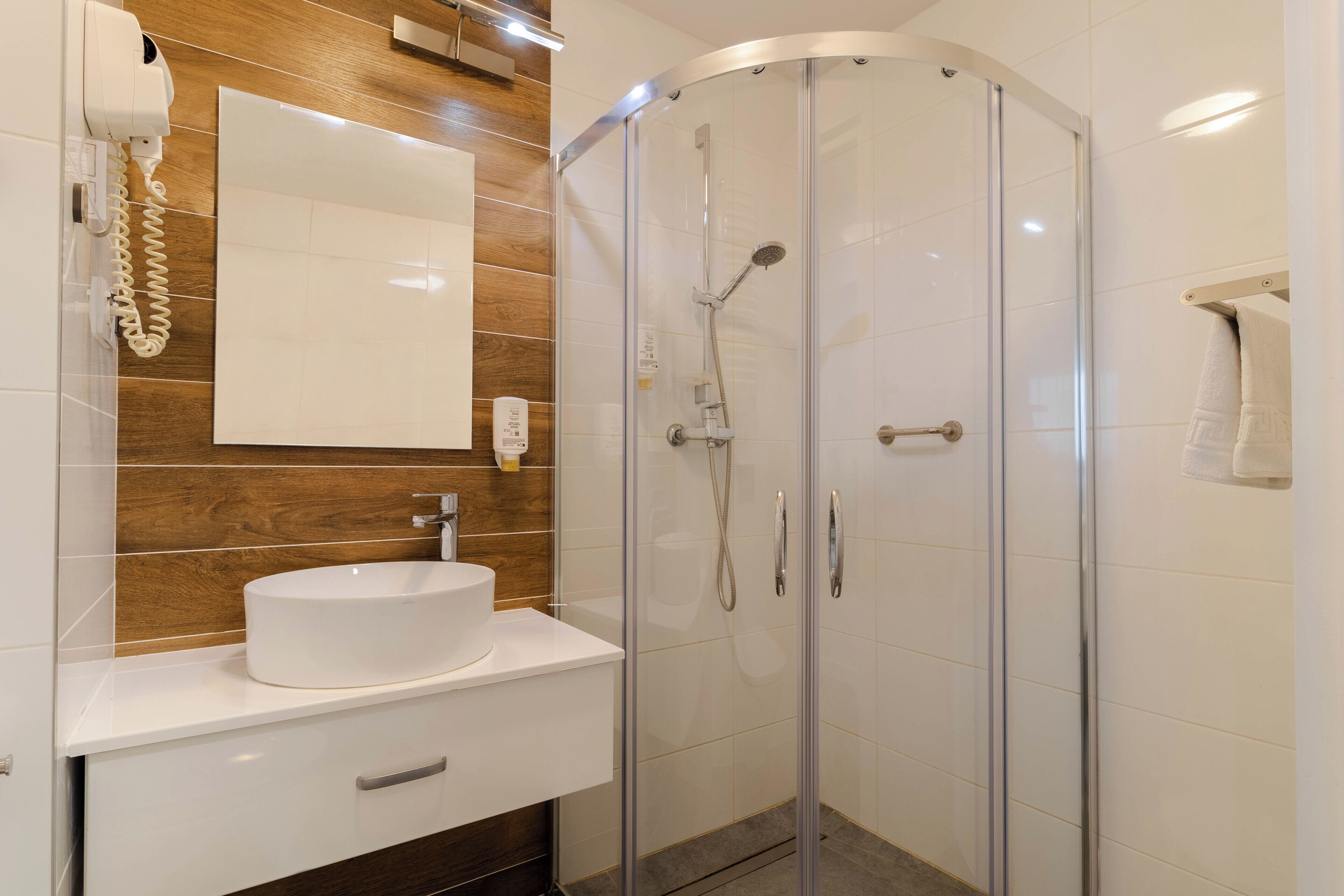 A modern bathroom with a glass-enclosed shower, a white sink, and a wooden accent wall.