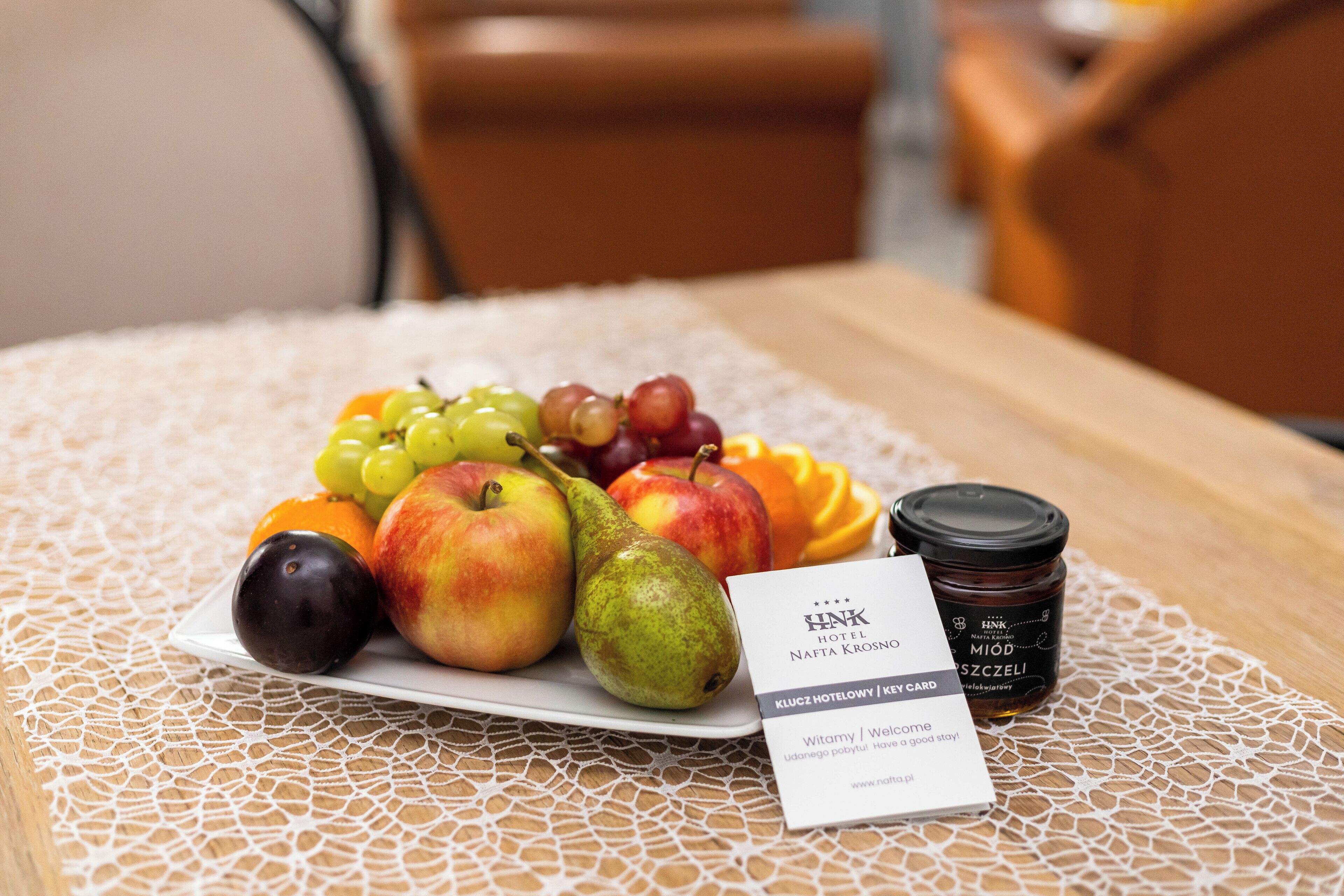 A table with a plate of fruit, a jar of honey, and a hotel business card.