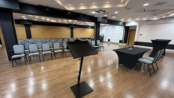 A conference room with rows of chairs, a black table, and a music stand.