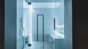 A modern, minimalist bathroom with a glass shower enclosure, a visible door, and a clean, tiled floor.