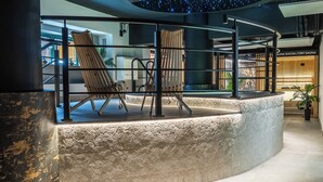 A modern lounge area with a stone wall, two wooden chairs, and a ceiling with a starry design.