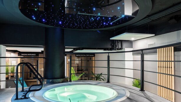 A modern spa area with a hot tub, a ceiling with star-like lights, and signs for 'SAUNA INFRARED' and 'SAUNA SUCHA / DRY SAUNA'.