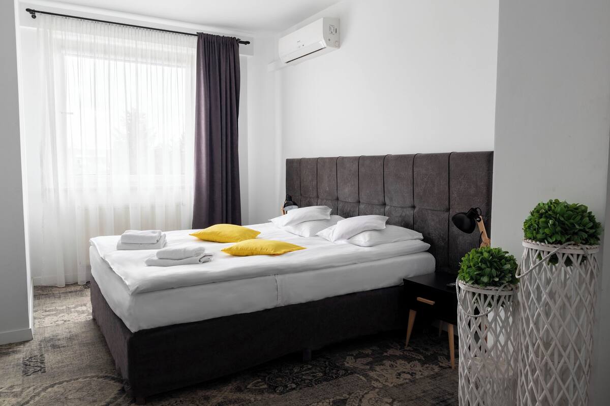 A neatly made bed with white linens and two yellow pillows, a dark headboard, and a small bedside table with a lamp.