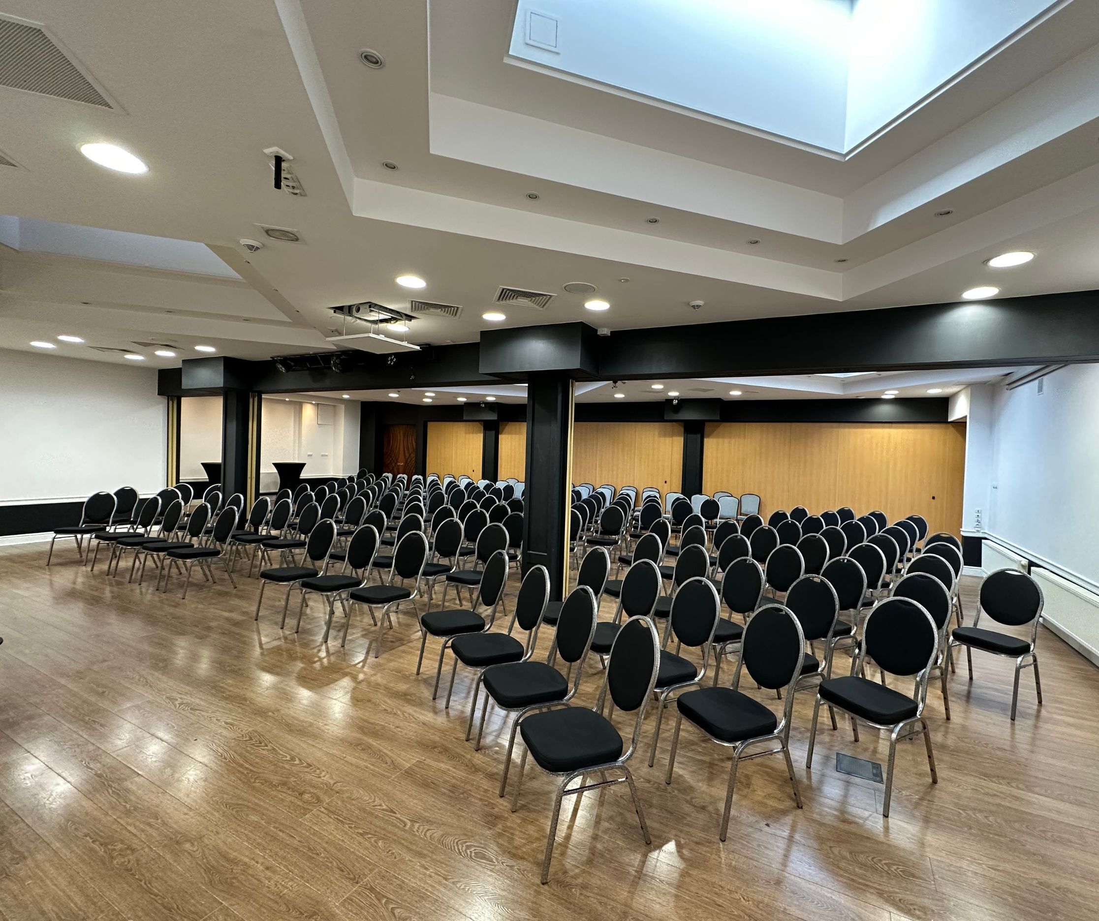 Un salón de conferencias con filas de sillas, un escenario y un tragaluz.