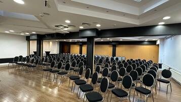 Een vergaderzaal met rijen stoelen, een podium en een dakraam.