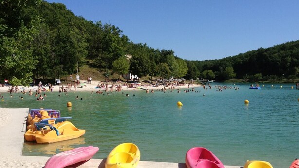 Une plage où l’on voit des gens nager et bronzer, et plusieurs kayaks jaunes et roses amarrés sur le rivage.