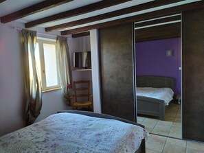 A bedroom with a bed, a chair, a wardrobe, and a window with curtains. - Country house with swimming pool (Beauville)