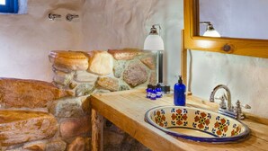 A rustic bathroom with a stone sink, wooden beams, and a large mirror.