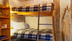 A rustic room with a bunk bed, wooden shelves, and a woven ceiling.