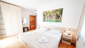 Een slaapkamer met een groot bed, een houten garderobe, een bureau, een stoel, een spiegel en een schilderij van een waterval.