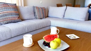 A modern living room with a grey sofa, patterned cushions, a wooden coffee table with a plate of fruit and a white mug.