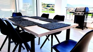 A dining area with a long table, black chairs, and a grill in the background.