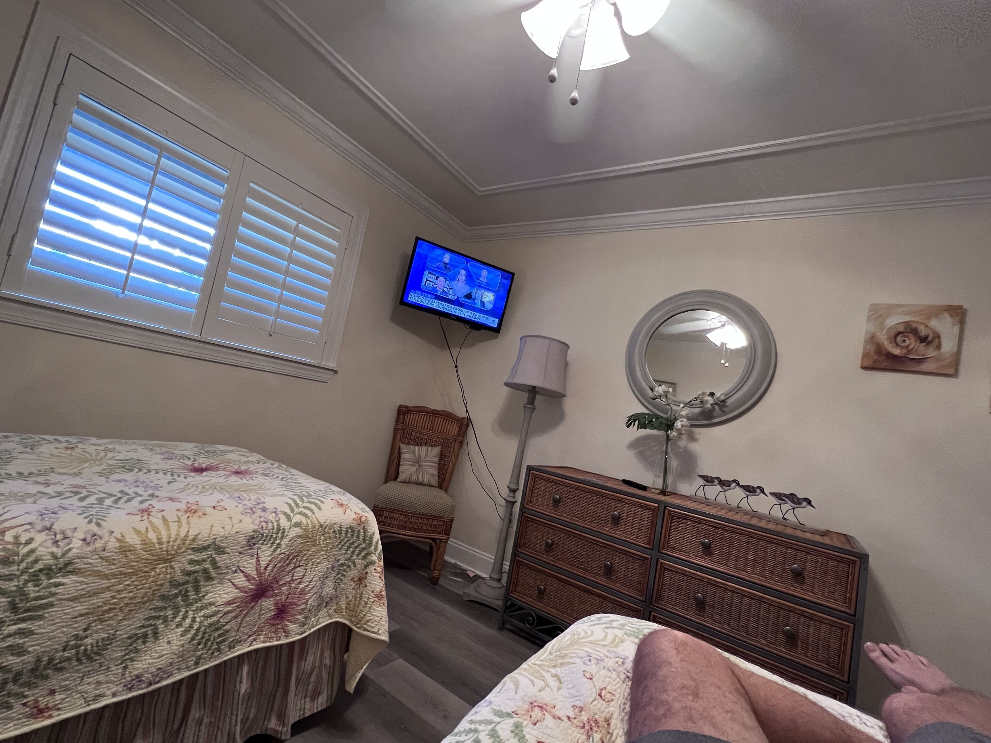 Ein Schlafzimmer mit Bett, Kommode, Fernseher und einem Fenster mit Jalousien.